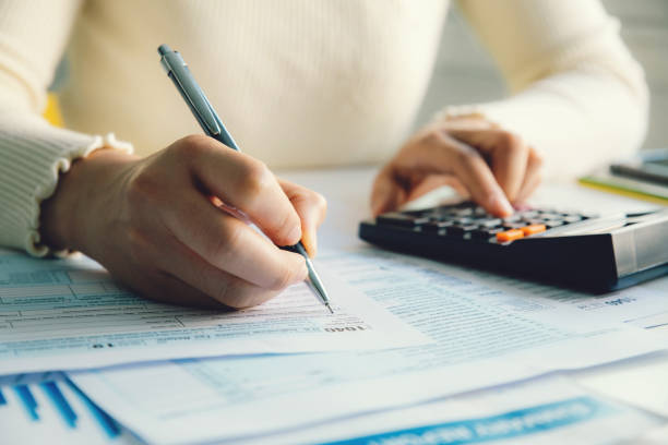 Person calculating tax using forms and a calculator, representing UK tax return preparation, financial documentation, and HMRC compliance.