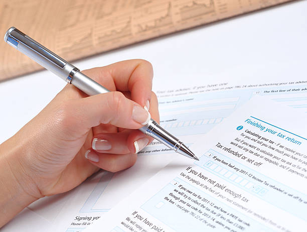 Close-up of a hand filling out a UK tax return form with a silver pen, symbolizing personal income tax reporting and compliance.